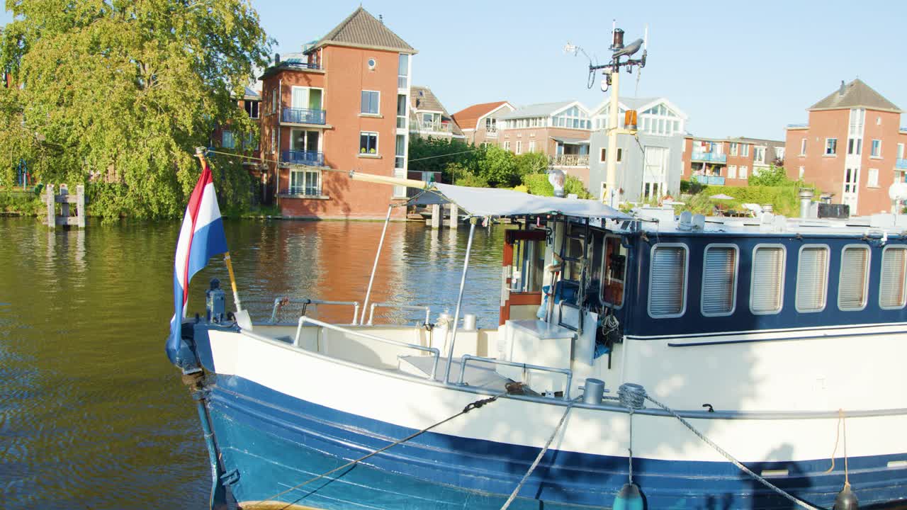 Blue and white boat with national flag glides along sunlit canal in historic Dutch city