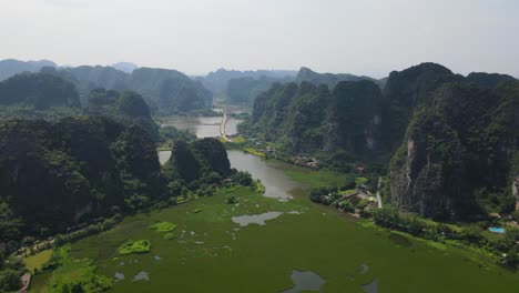 drone shot of beautiful green water-fern lake between jungle covered limestone mountain in ninh binh viet nam