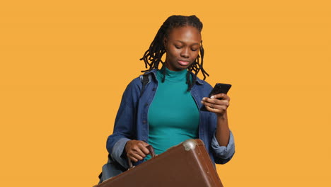 Smiling-girl-going-on-vacation-with-suitcase,-reading-texts,-studio-background