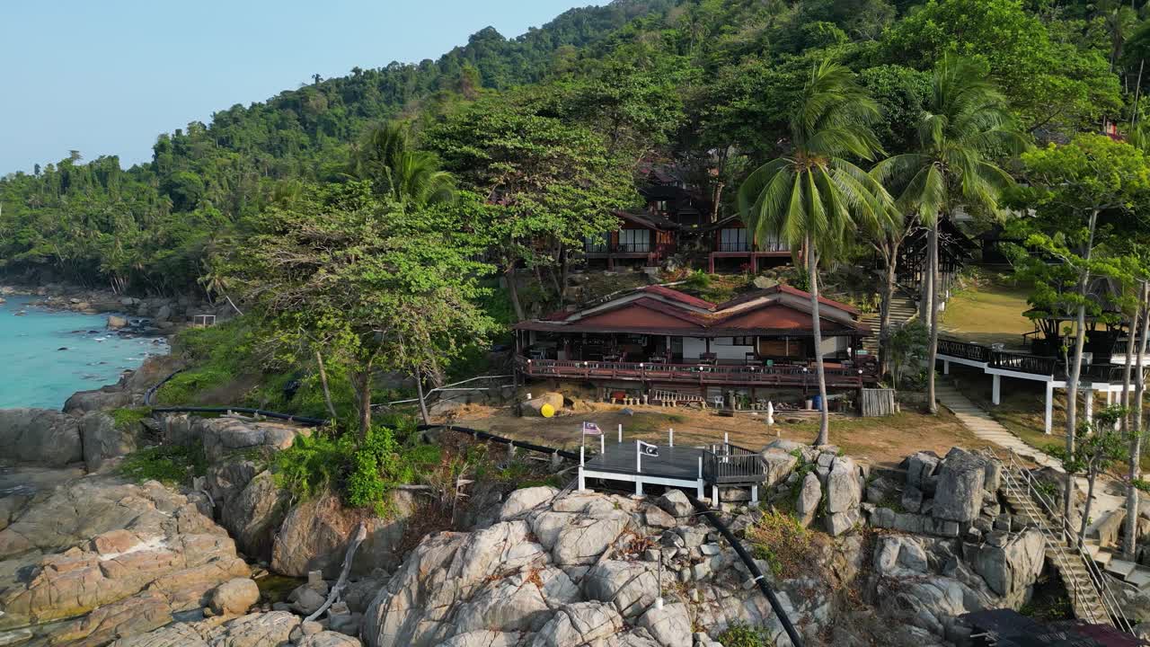 A stunning aerial view of a beach resort in Malaysia, surrounded by lush greenery and rocky shores overlooking the blue ocean. orbit motion