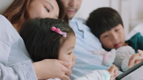 happy asian family using tablet computer at home mother and father with children watching entertainment playing game on touchscreen device learning having fun relaxing in bed 4k footage