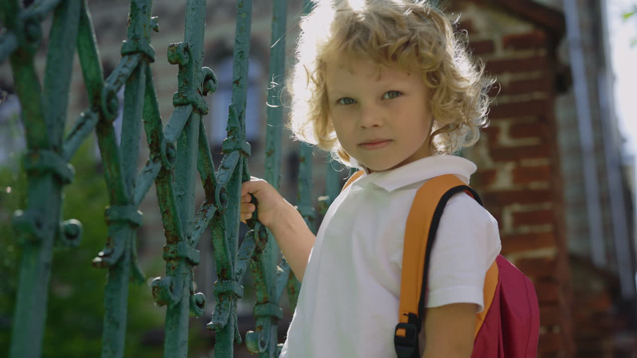 Boy with Backpack Leaning on a Fence