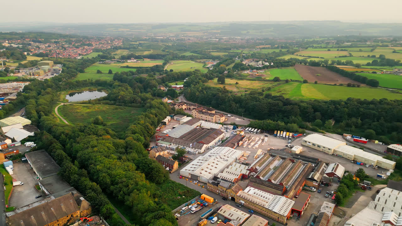 Drone-captured video of Heckmondwike, UK, reveals industrial structures, bustling streets, and an old town center against the Yorkshire backdrop on a summer evening