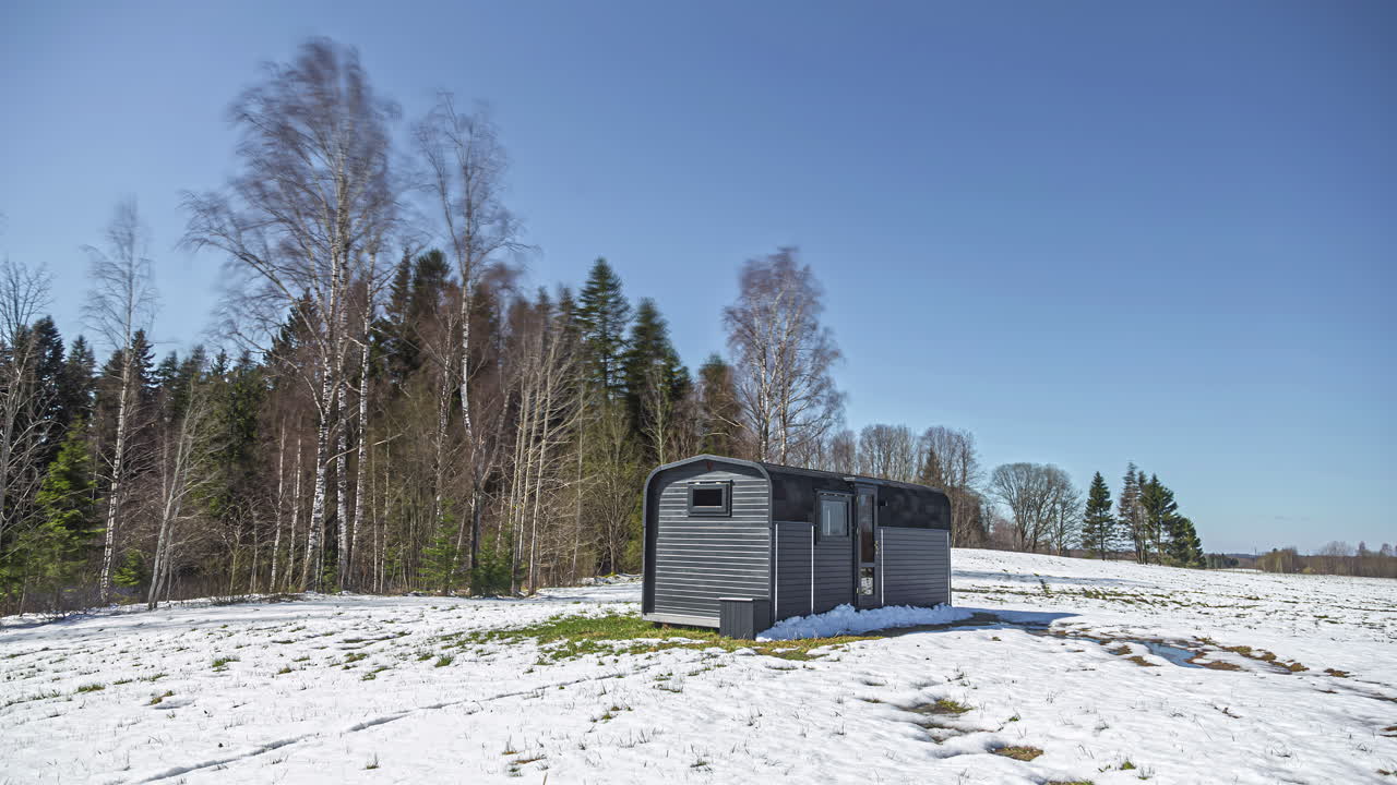 toma de tiempo de nieve derritiéndose alrededor de una cabaña de madera en un día nublado de invierno que indica la llegada de la primavera en el campo rural