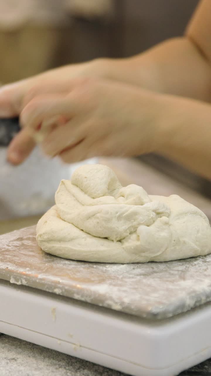 Fornaio che pesa l'impasto fresco su una bilancia in una cucina commerciale.