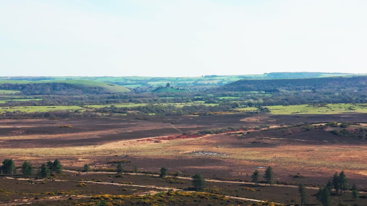 Bred udsigt over hedelandskab med bølgende bakker og lappetæppe af landbrugsmarker i blødt lys i Storbritannien.