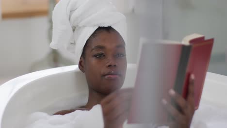 portrait of african american attractive woman relaxing in bath and reading book in bathroom