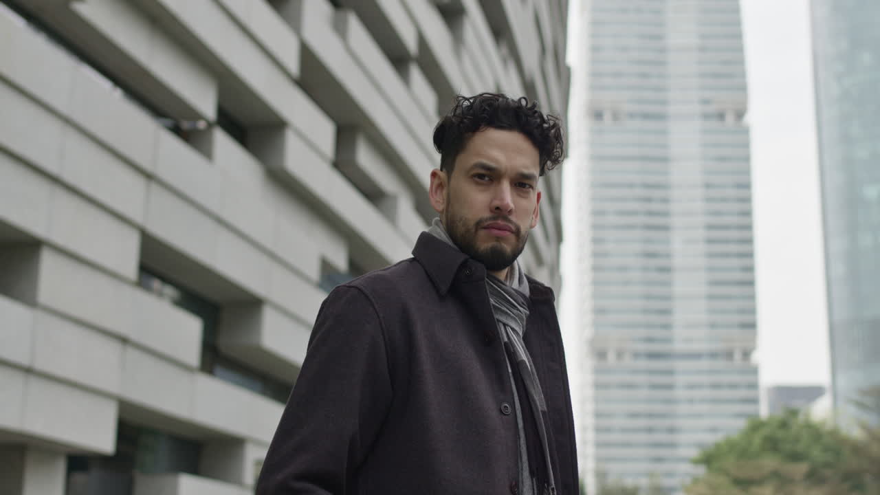 Portrait of successful young entrepreneur, dressed in autumn clothes, looking at camera serious and strong, outdoors in downtown business district