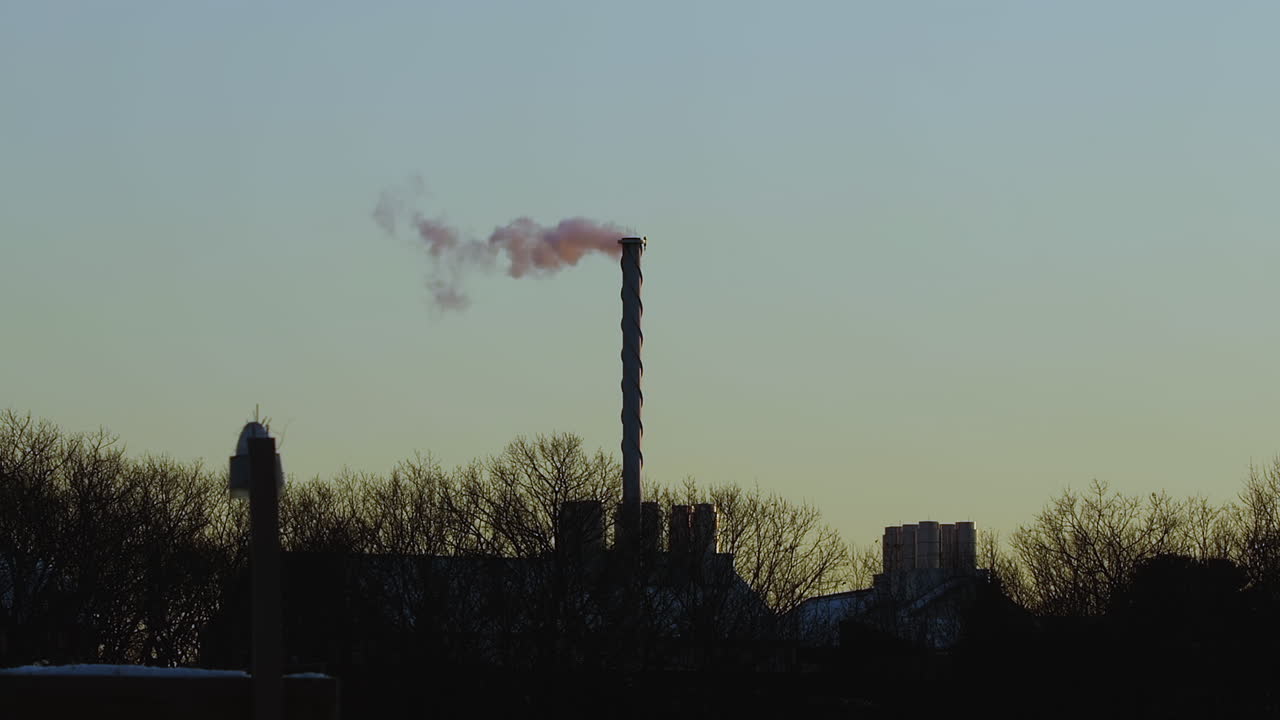 Steam billowing from tall exhaust stack after sunset, with a seagull flying by, during mid-winter, near Saco, Maine. Wide shot. Slow motion.