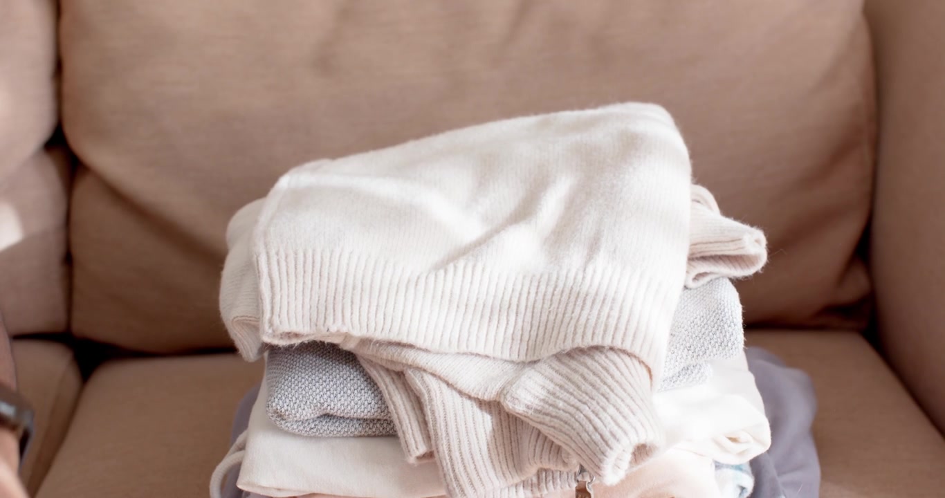 African American man seeing sweater reaching, pressing, folding sweaters on sofa to tidy