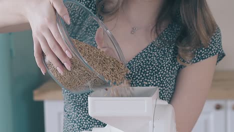 woman-pours-raw-grains-out-of-bowl-in-flour-mill-in-kitchen