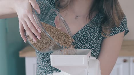 woman pours raw grains out of bowl in flour mill in kitchen