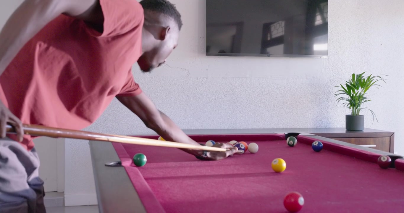 African adult entering frame in game room, inspecting rack, adjusting cue, lining up to break rack