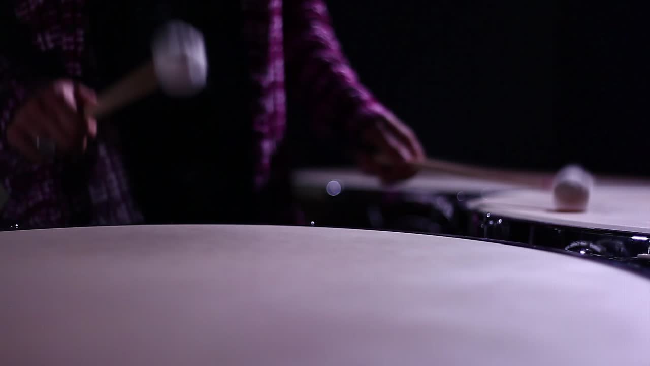 A man playing timpani in a dark room, close up.