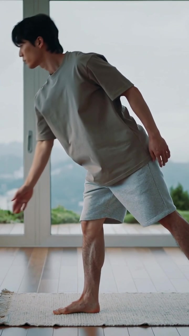 Vertical video: Leaning man shifting weight for balance in living room by windows on rug, barefoot