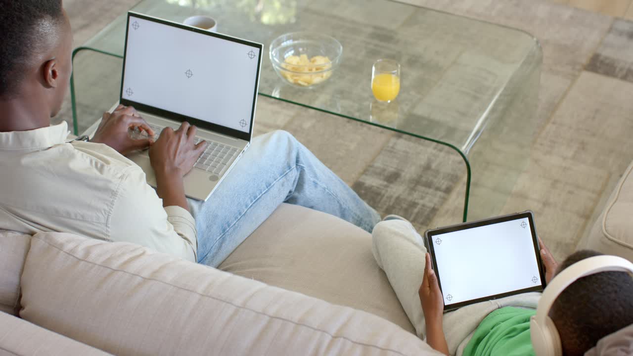 Clip is starting; adult typing on laptop for work, child watching tablet for play on sofa