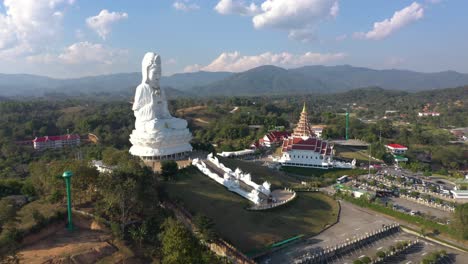 aerial drone flying towards wat huay pla kang giant white big statue and pagoda temple with mountains and landspace in chiang rai, thailand