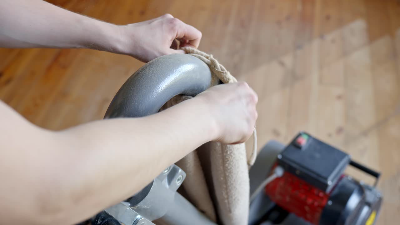 Person’s hands replace the sanding waste bag on a floor sanding machine in a room with pine wooden floor, showing the maintenance process and details of the tool, clear light, static camera, close up