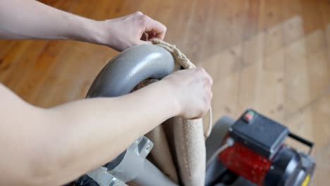 person’s hands replace the sanding waste bag on a floor sanding machine in a room with pine wooden floor, showing the maintenance process and details of the tool, clear light, static camera, close up