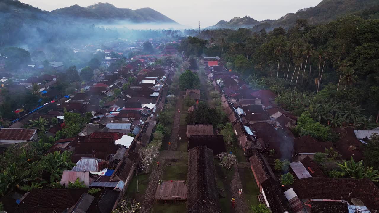 Scenic drone video of a traditional Indonesian village in a lush valley showing wooden houses with thatched roofs and historical architecture that reflects rural lifestyle and ancient culture