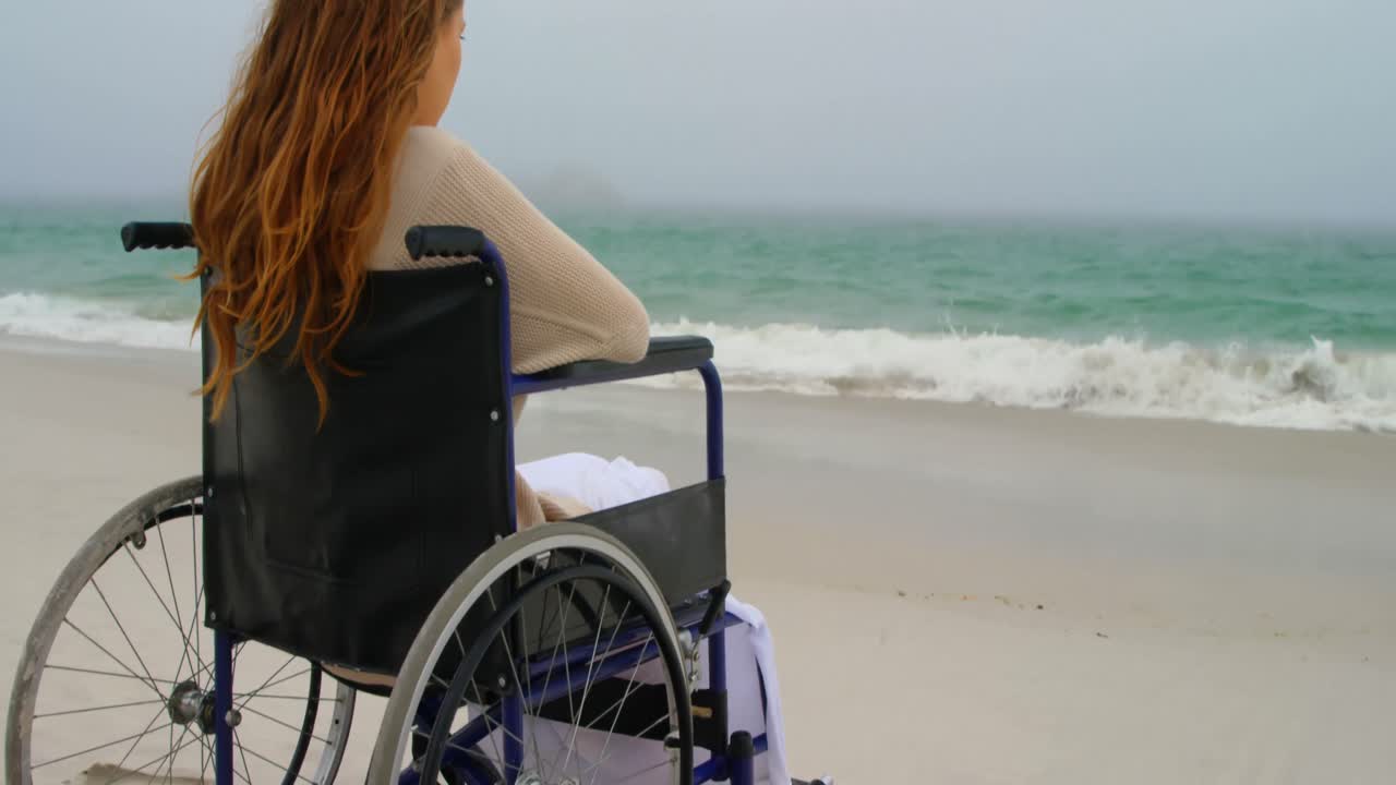 Rear view of woman sitting on wheelchair at beach 4k