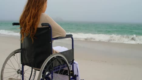 vista trasera de una mujer sentada en silla de ruedas en la playa 4k