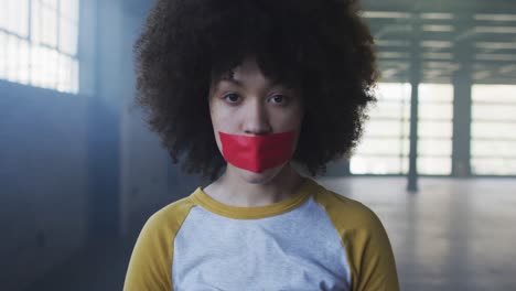 Portrait-of-african-american-woman-with-red-tape-on-her-mouth-in-empty-parking-garage