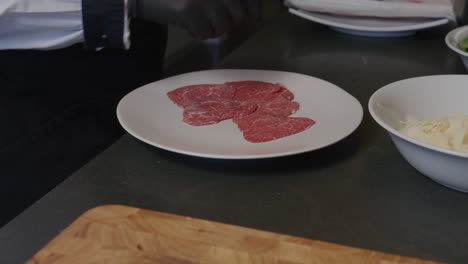 un chef meticulosamente capas de carne de res japonesa a5 wagyu en un plato blanco crujiente