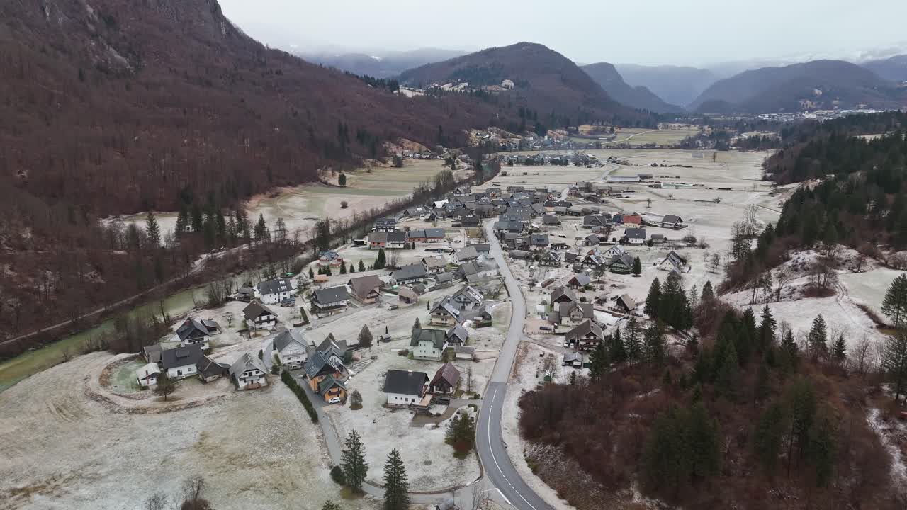 Kamnje, tradycyjna alpejska wioska w Parku Narodowym Triglav w Słowenii, położona wśród zaśnieżonych łąk, lasów i rzeki Sava Bohinjka, widziana z podwyższonej perspektywy lotniczej zimą.