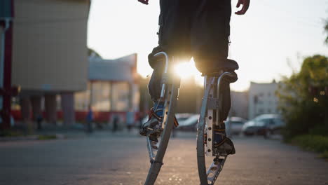 back view of person walking on spring stilts during sunset wearing gray hoodie and pants. background features blurred trees, suburban street, and warm sunlight creating soft shadows