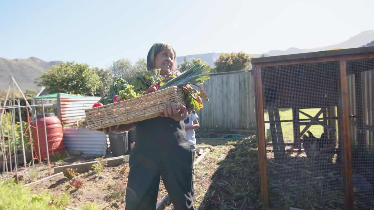 은 정원에서 채소 바구니를 들고 있는 두 인종의 할머니와 손자, 느린 동작