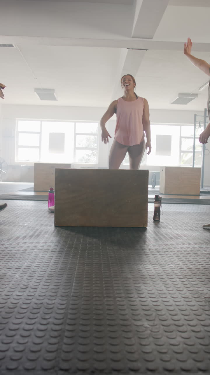 Vertical video of diverse sportswomen exercising and high fiving at gym in slow motion