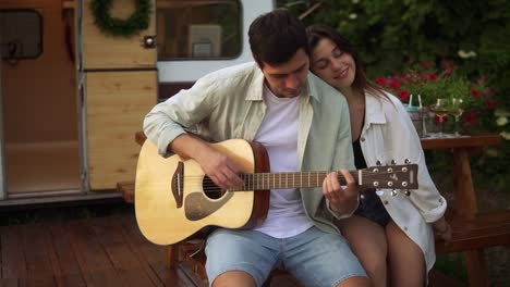 una pareja romántica sentada al aire libre frente a su furgoneta y un hombre tocando la guitarra para su novia. al aire libre. una chica escuchando música y abrazando a un hombre. cámara lenta