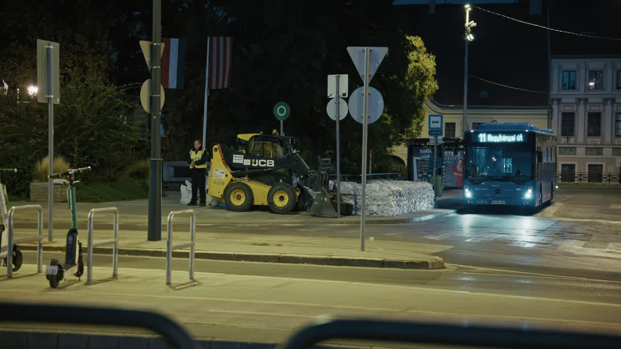 Construction vehicle and bus at night near flood barriers, Budapest Flood 2024 scene