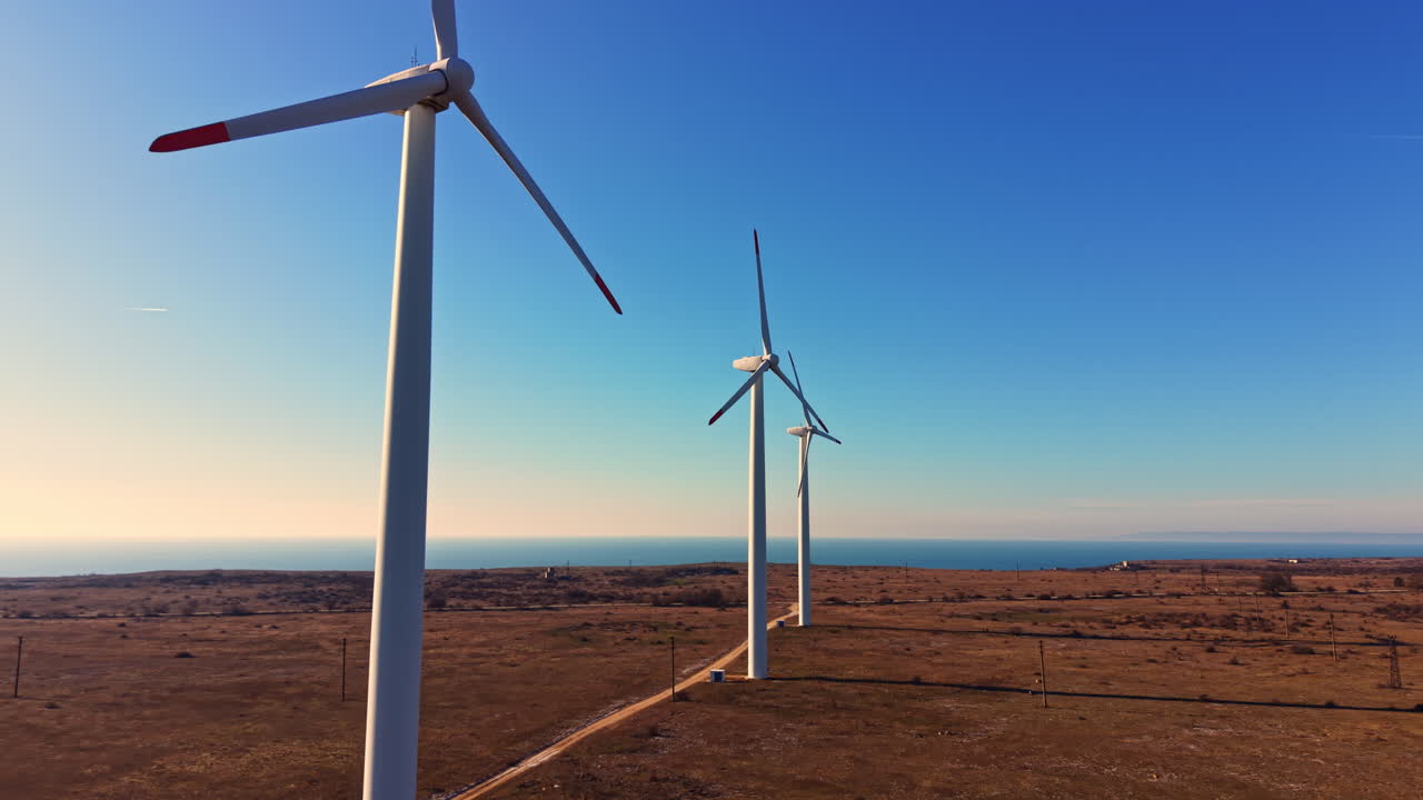 Turbine eoliche si ergono alte contro un cielo sereno vicino alla costa in un paesaggio aperto durante il giorno