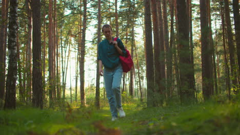 mujer excursionista caminando a través de un bosque sereno, llevando una bolsa roja sobre el hombro, pareciendo cansada pero decidida, la luz del sol se filtra suavemente a través de los árboles altos, arrojando un brillo cálido