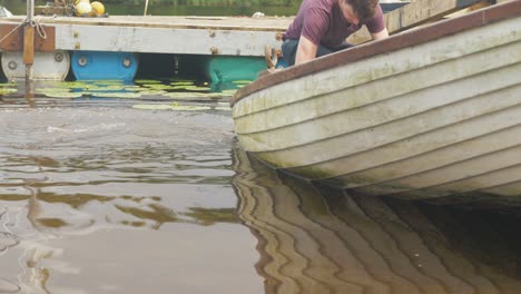 Junger-Mann-Schöpft-Wasser-Aus-Fiberglas-Fischerboot