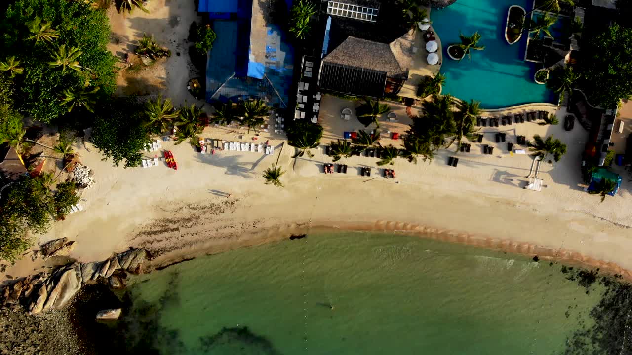 una fotografía aérea de un dron que se desplaza hacia la playa de la bahía de thongson, donde los bañistas están nadando y tomando el sol frente a uno de los resorts aislados de la isla de koh samui, tailandia.