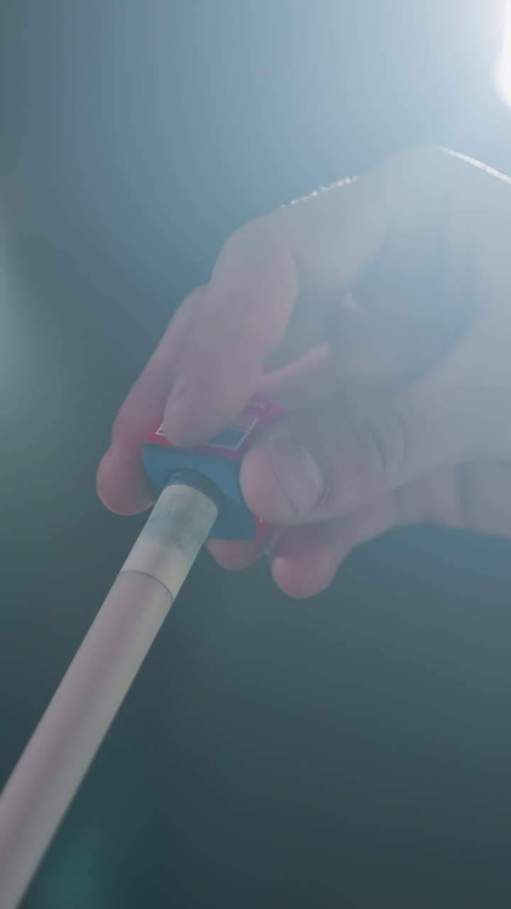 손가락이 조심스럽게 빨간색과 파란색 도자기를 빌리어드 게임 전에 큐 스틱에 적용하는 클로즈업. 집중된 손잡이와 흐릿한 배경은 정밀성, 집중력을 강조합니다.