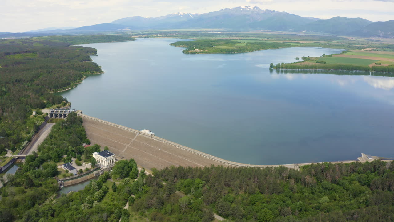 Pedestal drone shot tilting downwards while showing the mountains, lake, and the Koprinka Dam in Central Bulgaria.