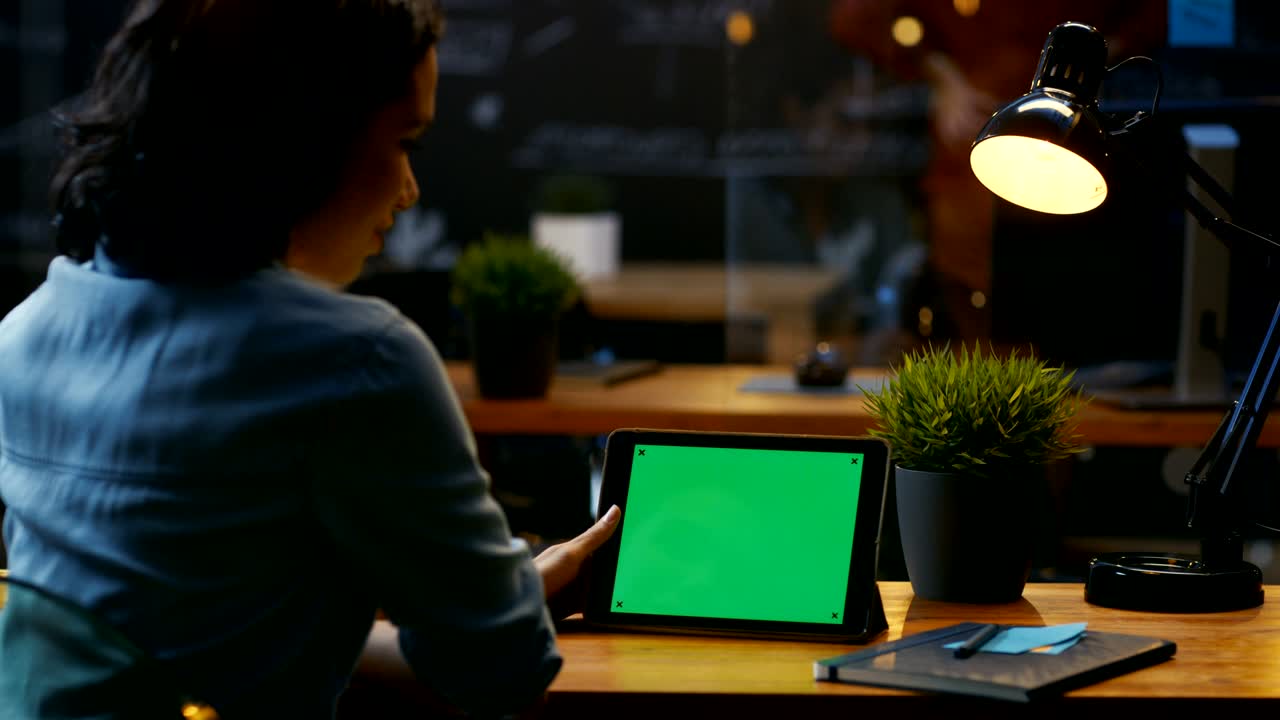 젊은 여성은 나무 책상에 앉아 풍경 뷰에서 모형 녹색 화면으로 태블릿 컴퓨터를 사용합니다.