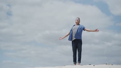 Happy-senior-caucasian-man-walking-barefoot-on-tropical-beach-and-raising-arms,-in-slow-motion