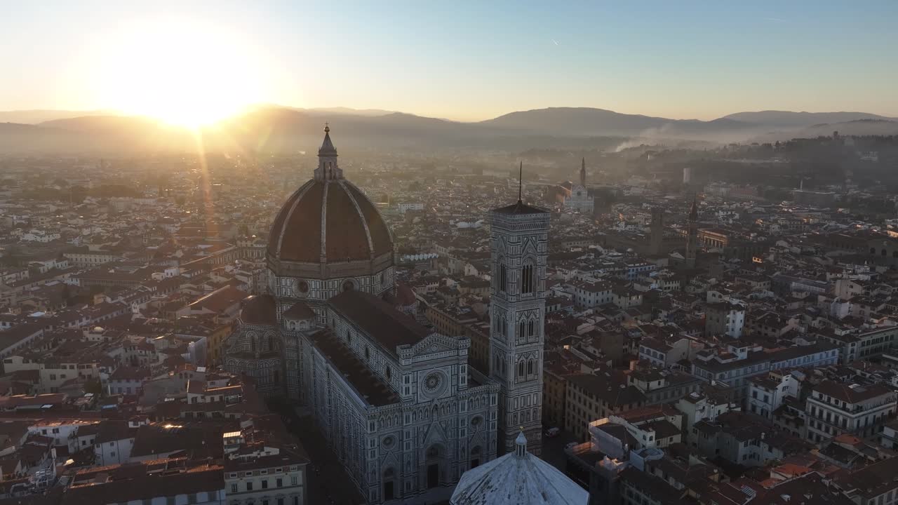 Wide high-angle aerial view of the Florence Cathedral, Giotto's Bell Tower, and the dense historical city center at golden hour sunrise