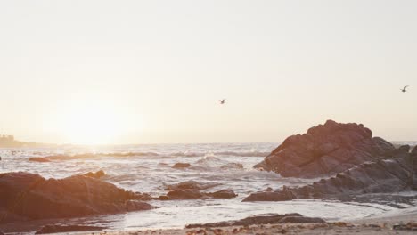 Beach-landscape-with-sea,-rocks-and-blue-sky-at-sundown,-in-slow-motion