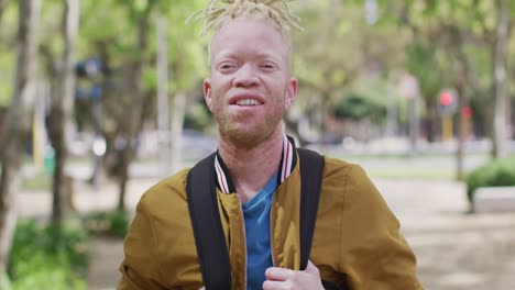 portrait of smiling albino african american man with dreadlocks in park looking at camera