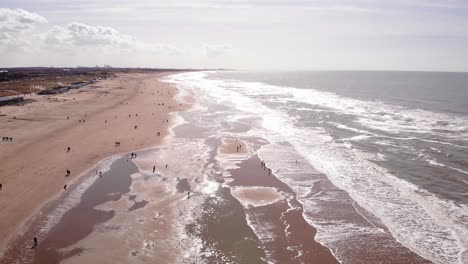 vuelo aéreo a lo largo de la costa de la playa de katwijk aan zee en un día soleado con gente repartida