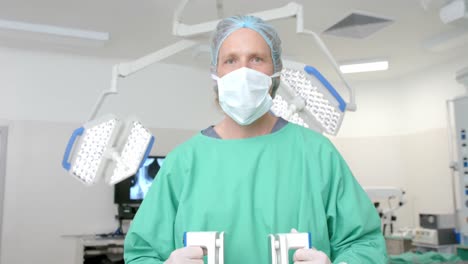 Portrait-of-caucasian-male-surgeon-wearing-surgical-gown,-holding-defibrillator,-slow-motion