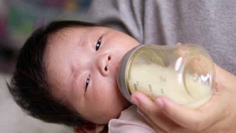 mother feeding her newborn child some infant formula in a feeding bottle that is being held by her mother