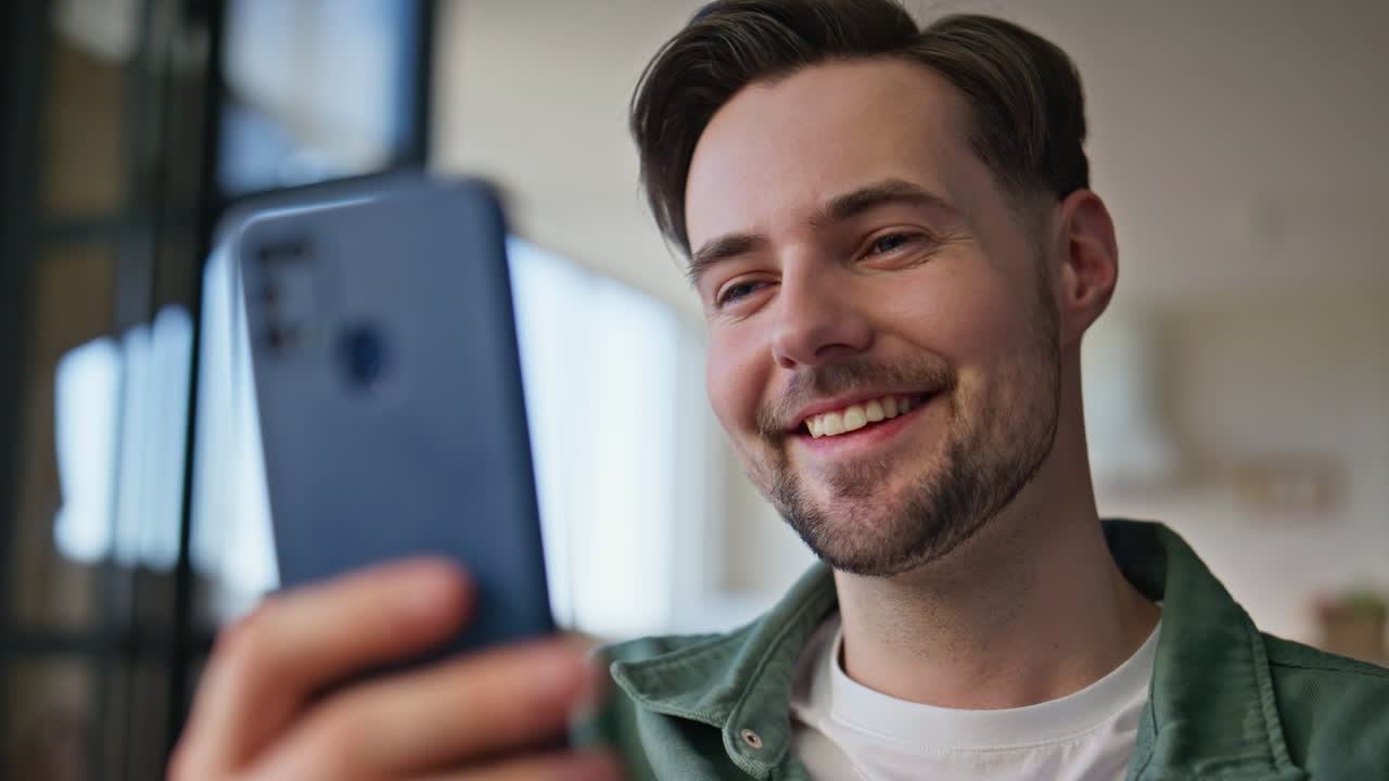 Cheerful student looking cellphone home closeup. Happy man watching smartphone