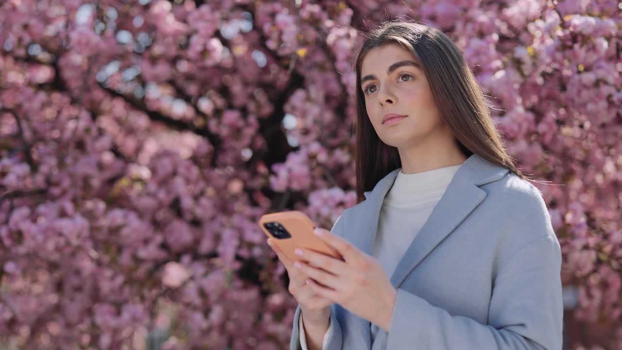Woman using smartphone under cherry blossoms